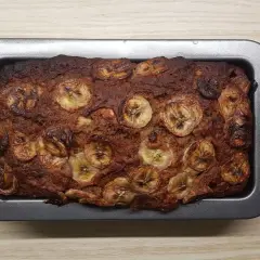 Upieczony proteinowy chlebek bananowy z plasterkami banana na wierzchu, w metalowej formie.