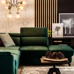 Wygodna, ciemno zielona kanapa w salonie z ozdobnymi poduszkami i lampą w stylu retro.