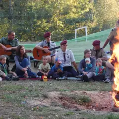 Ognisko i gitary tworzą atmosferę do wspólnego śpiewania piosenek obozowych. Dzieci i dorośli siedzą razem, słuchając muzyki.