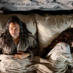 Un homme aux longs cheveux regarde la caméra, allongé dans un lit à côté d'une femme endormie. Un air de mystère plane sur ce moment, rappelant les intrigues de Mordred dans Kaamelott.