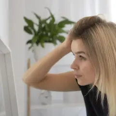 Kobieta z blond włosami sprawdza w lustrze, czy jej skóra głowy nie jest podrażniona po użyciu szamponu z **sodium lauryl sulfate**.