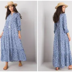 Modelka prezentuje zwiewną, błękitną sukienkę w drobne kwiatki, idealną dla kobiet plus size. Długi fason i falbany dodają jej lekkości.