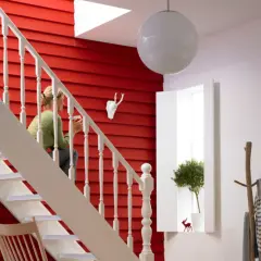Ein rotes, holzvertäfeltes Treppenhaus mit weißer Balustrade. Eine Frau sitzt auf der Treppe. Ein Hirschkopf und ein Baum schmücken die Wand. So lässt sich ein Treppenhaus gestalten.