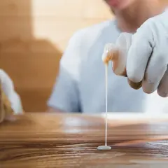 Application d'un produit sur un bois, peut-être pour effacer une tache blanche laissée par un plat chaud.