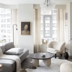A cozy living room, perfect for learning how to furnish a small apartment. A grey sofa, fluffy armchair, and round coffee table create a welcoming space.
