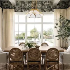 A bright dining room in a Studio McGee home features a large wooden table with rattan chairs, plush armchairs, and a floral wallpaper.