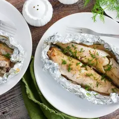 Dwa pieczone mintaje w folii aluminiowej, posypane koperkiem. Prosty i pyszny mintaj przepis.