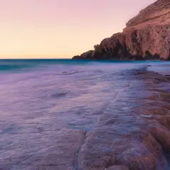 El mar acaricia las rocas de la cala el corral carboneras al atardecer, creando un paisaje sereno y etéreo.