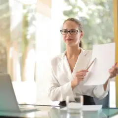 Kobieta w okularach, trzymająca dokument i ołówek, wyjaśnia, kto to prokurent.