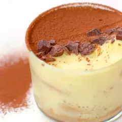 Delizioso tiramisù fatto in casa in un bicchiere, cosparso di cacao e scaglie di cioccolato.
