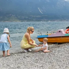 Mama z dziećmi na kamienistej plaży nad jeziorem. W tle góry i kolorowe łódki. Wspaniały dzień nad Gardno.