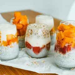 Sześć deserów z nasion chia, jogurtu i owoców (truskawki, mango) w szklankach.