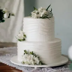 Elegancki tort komunijny, idealny na 20 osób. Białe kwiaty zdobią dwupoziomowe ciasto.