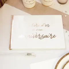 Un livre d'or de mon anniversaire, prêt à recueillir les vœux les plus doux. Un stylo blanc et des décorations dorées complètent la scène festive.