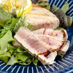 Saftiges Thunfisch Steak, medium gebraten, serviert mit frischem Salat, Dill und einer Zitronenspalte auf einem blauen Teller.
