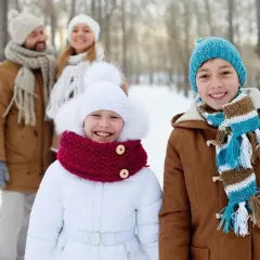 Familia sonriendo en un día de **invierno para niños**. Los niños al frente llevan abrigos y bufandas coloridas.