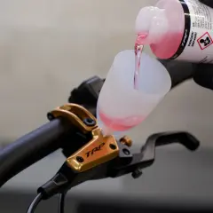 Adding brake fluid without bleeding is not recommended. This image shows pink fluid being poured into a funnel on a TRP brake lever.