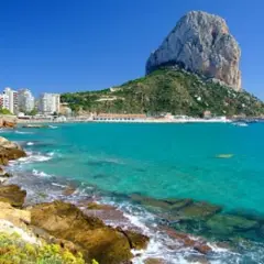 Vista del natural park of Penyal d'Ifac con aguas turquesas, rocas y edificios costeros.
