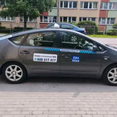 Szary hybrydowy Prius z napisem "284 KOSZALIN" i numerem telefonu do zamówienia taksówki.