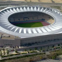 Imponujące, okrągłe **Estadio La Cartuja** z charakterystycznym, falującym dachem, otoczone zielenią i drogami.