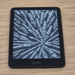 Un Kindle, une liseuse électronique affichant une image abstraite de plumes d'encre, sur un fond en bois.