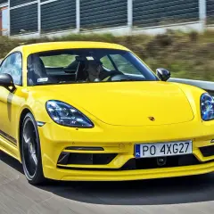 Żółty Porsche Cayman T pędzi po drodze, kierowca w czapce z daszkiem za kierownicą.