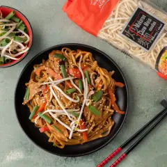 Genialny makaron chiński z kurczakiem przepis: danie z kurczakiem, warzywami i kiełkami fasoli mung, obok paczka makaronu chow mein.