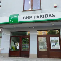 Wejście do placówki banku BNP Paribas z zielonym logo i napisem. Obok drzwi znajduje się bankomat.