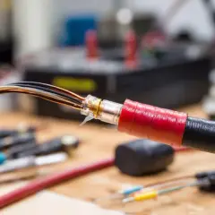 Przewody z odsłoniętymi żyłami, zabezpieczone taśmą izolacyjną. W tle widać narzędzia i sprzęt elektroniczny.
