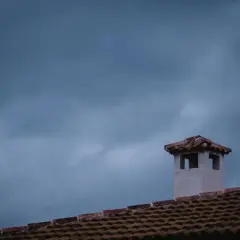 Komin na dachu, jakby pokryty folią w płynie, na tle burzowego nieba.
