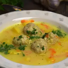 Zupa klopsowa babci: pyszne klopsiki w żółtym, kremowym sosie z ziemniakami i marchewką, posypana natką pietruszki.