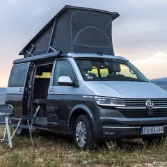 Szary kamper VW California z podniesionym dachem, idealny na wakacje. Poznaj jego wymiary i możliwości podróżnicze.