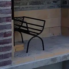 En grill under uppbyggnad av tegelstenar. En svart metallbänk står inne i den tomma eldstaden.