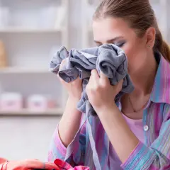 Kobieta wącha ubranie, które śmierdzi stęchlizną.