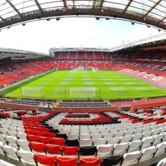 Widok na pusty stadion Old Trafford, z zieloną murawą i rzędami czerwonych, białych i czarnych siedzeń. Imponująca old trafford pojemność robi wrażenie.