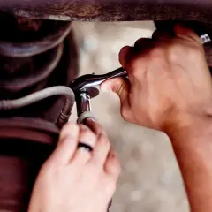 Ręce z kluczem nasadowym próbują odkręcić wyrobioną śrubę imbusową, która jest częścią mechanizmu samochodowego.