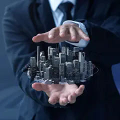 Biznesmen trzyma w dłoniach futurystyczne miasto, symbolizujące inwestycje i rozwój. To właśnie co to są reity - inwestycje w nieruchomości.
