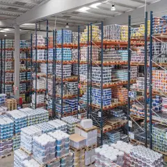 Großes Lager mit vielen Regalen voller Farbeimer und anderer Arbeitsmittel. Ein Gabelstapler steht bereit.