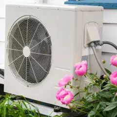 Unità esterna di una pompa di calore ad aria, con fiori rosa in primo piano.