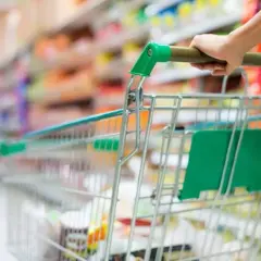 Ręka pcha wózek sklepowy w alejkach sklepu spożywczego, tworząc obraz dynamicznego doświadczenia w branży retail.