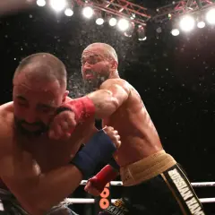 En slagväxling i MMA-ringen. En fighter med röd lindning på handen levererar en kraftfull träff mot motståndarens ansikte. Kanske är detta den bästa MMA-fightern i aktion.