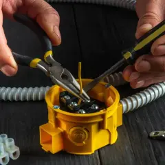 Ręce majsterkowicza wykonują wymianę puszki elektrycznej, używając szczypiec i śrubokręta do podłączenia przewodów.