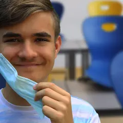 Joven sonriente se quita mascarilla, recordando la importancia de conocer los **covid en niños sintomas** para su bienestar.