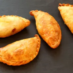 Cuatro empanadillas doradas y crujientes, recién hechas en freidora de aire, reposan sobre una pizarra oscura.