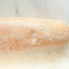 Chleb rustykalny, lekko oprószony mąką, z chrupiącą skórką, gotowy do krojenia.
