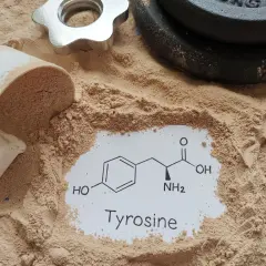 Proszek proteinowy, miarka i ciężarki. Na białej kartce wzór chemiczny i napis "Tyrosine". Tyrozyna co to? Aminokwas wspierający trening.