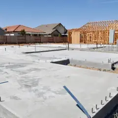 Fundament domu z chudego betonu, gotowy pod budowę ścian. W tle widać konstrukcję szkieletową domu.