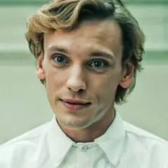 Jamie Campbell Bower, aktor wcielający się w postać Vecny, z niebieskimi oczami i blond włosami, w białej koszuli.