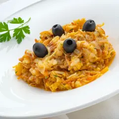 Delicioso revuelto de bacalao con aceitunas negras y perejil fresco, servido en un plato blanco.