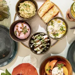 Un plateau de mezzés colorés, avec des dips crémeux, des toasts et une salade de tomates. Les belles plantes aromatiques ajoutent une touche de fraîcheur.